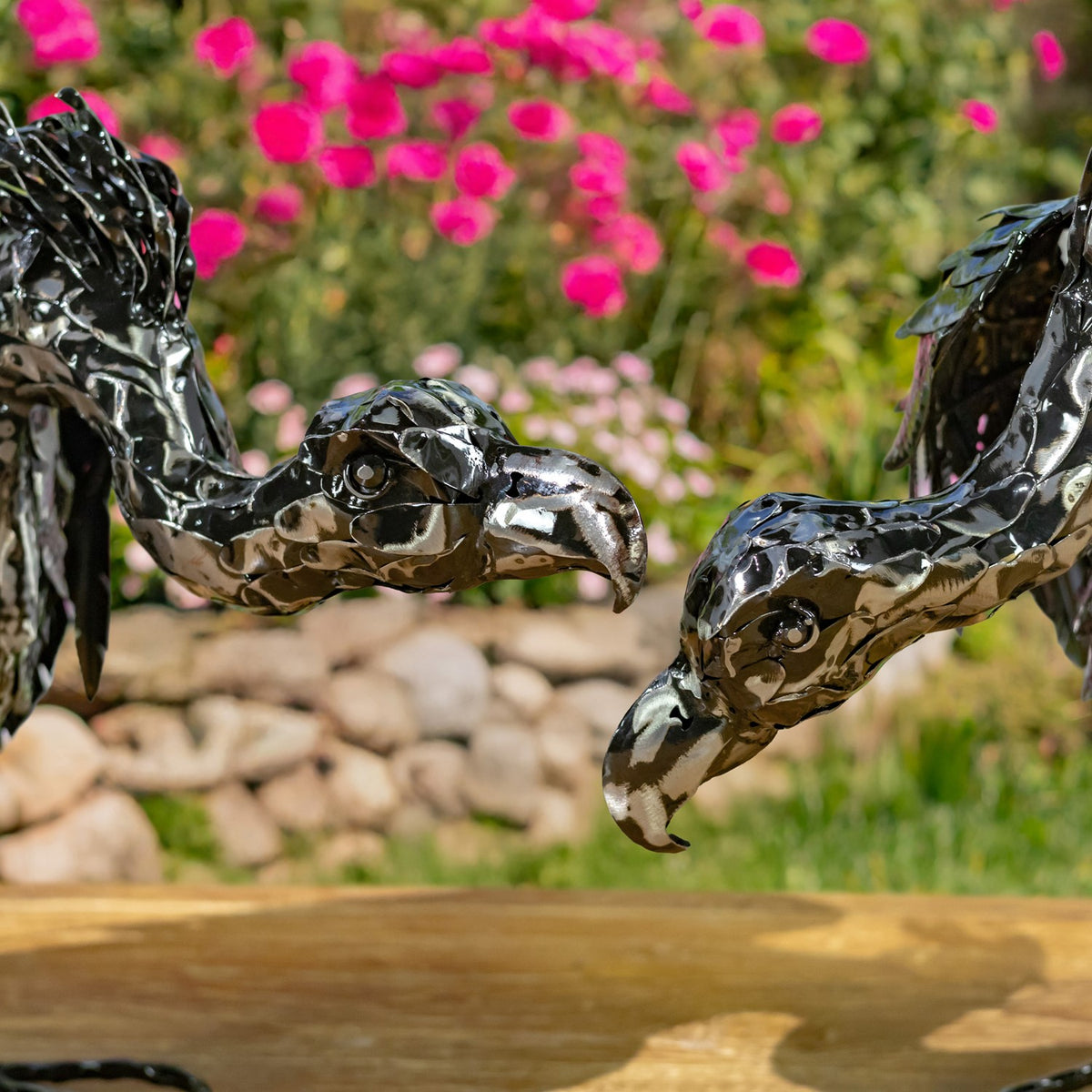 Close view of two metallic vulture heads with curved beaks in a garden