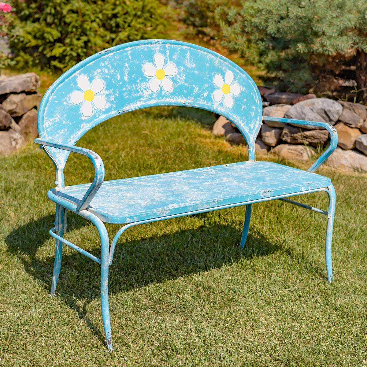 Blue metal garden bench with a curved back, white flower accents, and a distressed finish on a lawn.