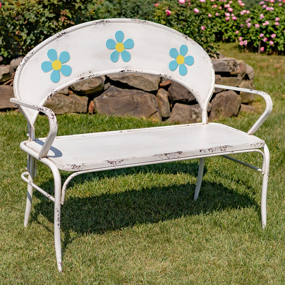 Closer view of a white garden bench with blue and yellow flowers across its curved back.