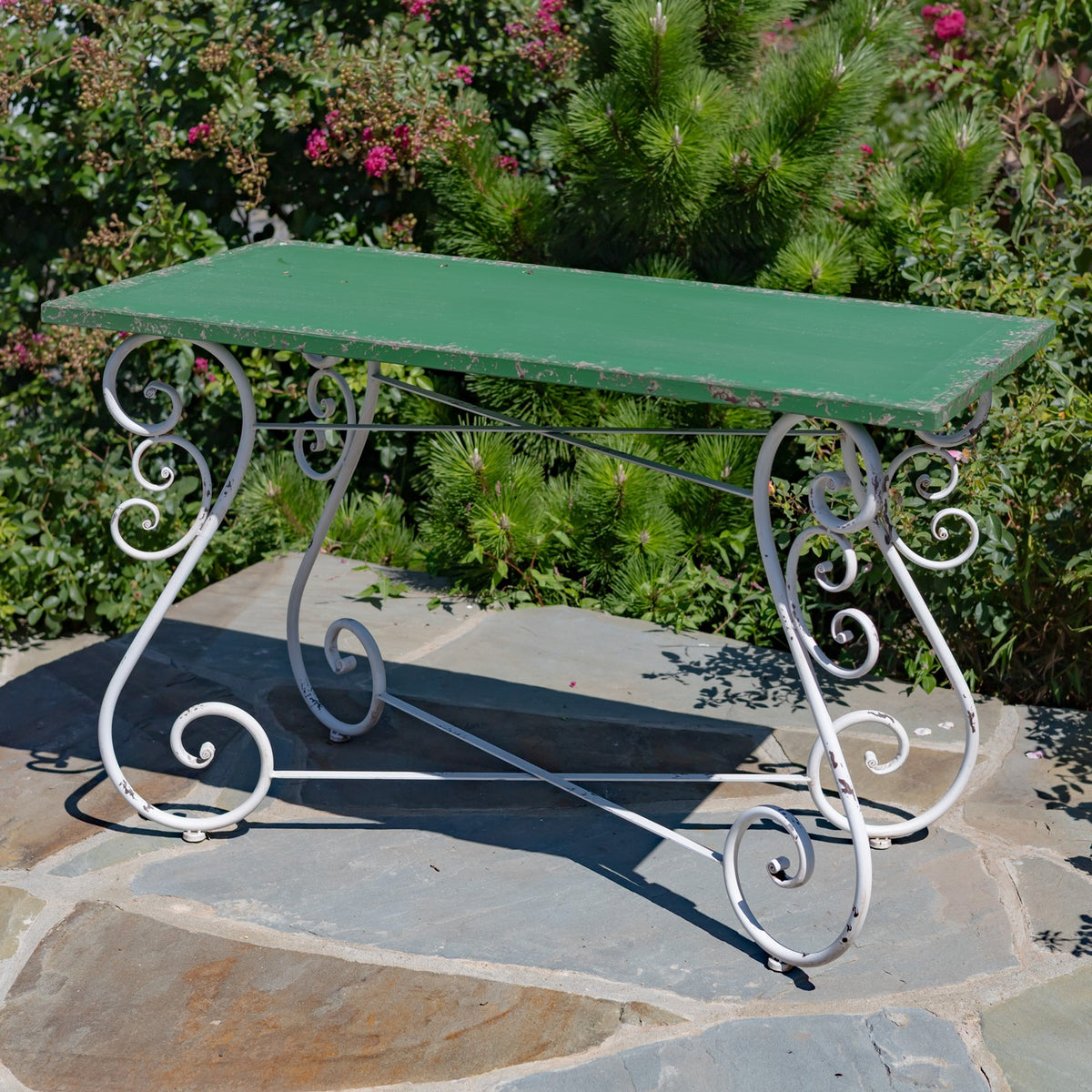 Green table shown from the side, with decorative curled metal supports and crossbars beneath the top.