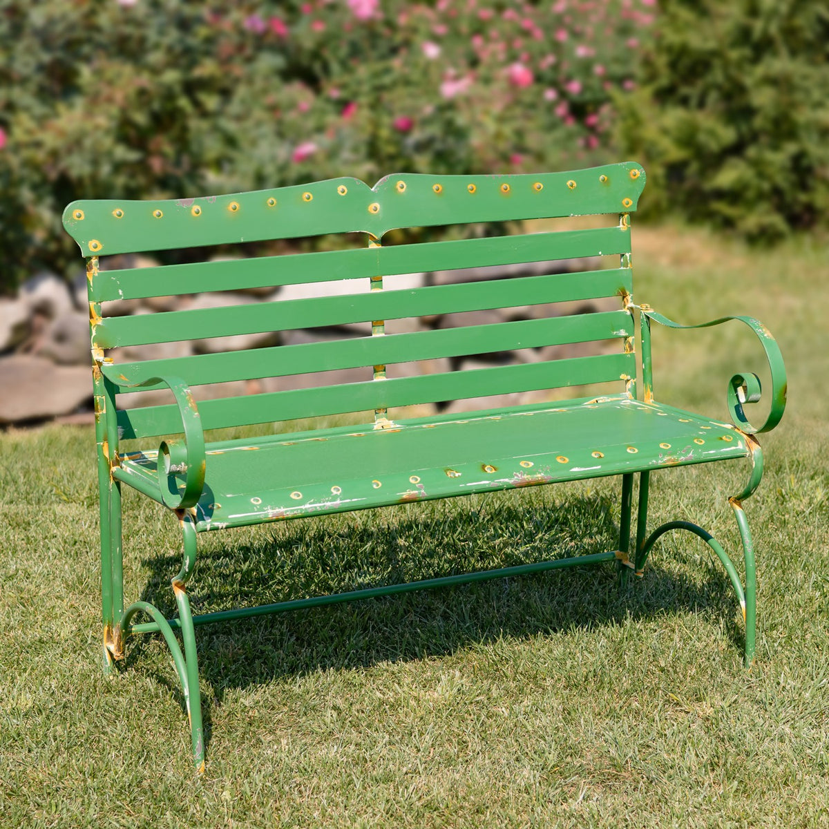 Green garden bench shown from the opposite angle, with decorative scroll arms and a slatted back.
