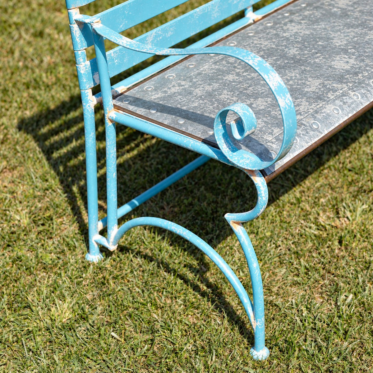 Close-up of a blue bench’s curled arm, curved leg, and gray metal seat.