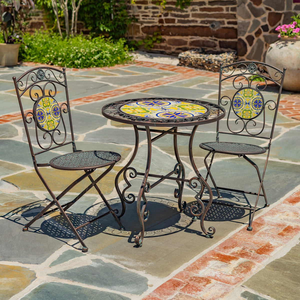 A round patterned table and two matching metal chairs arranged on a flagstone patio.