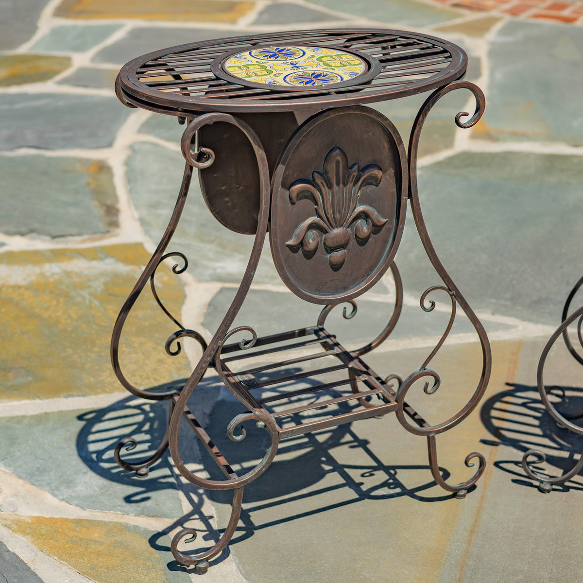 A dark metal plant stand with curled legs, a raised floral panel, and a colorful round mosaic top.