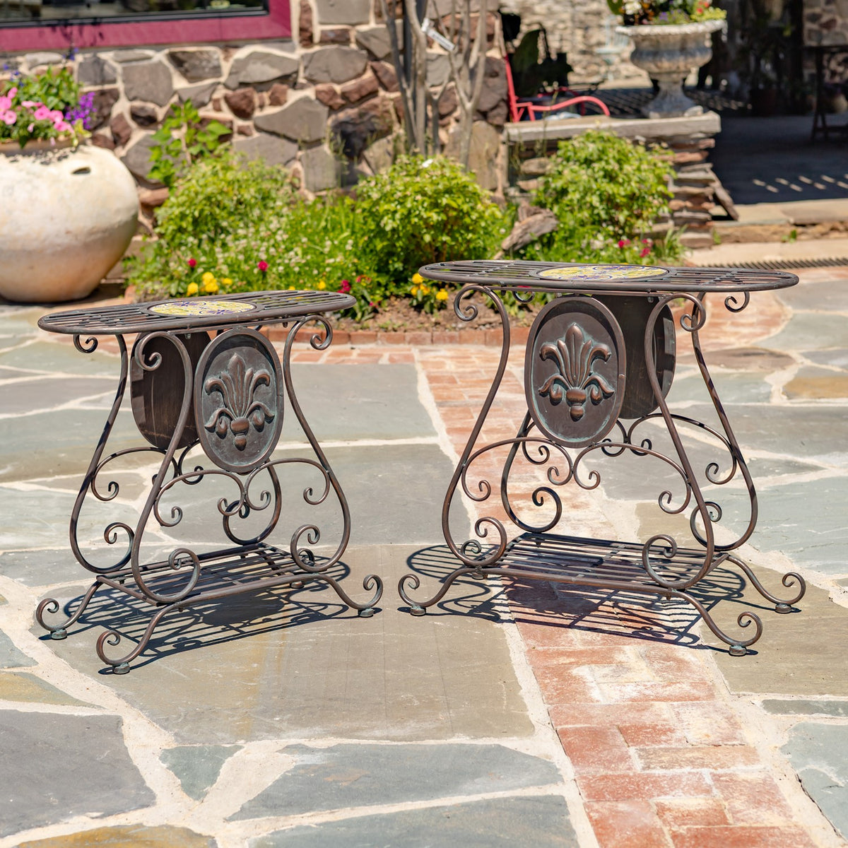 Pair of scrollwork metal plant stands with oval fleur-de-lis panels and slatted shelves.
