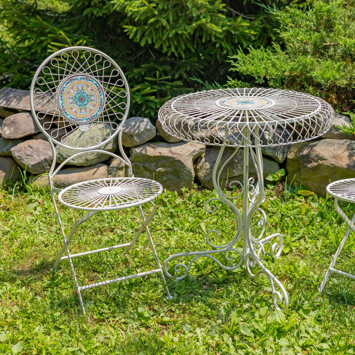 Closer angled view of the wire bistro set, with one chair beside the round mosaic-topped table.