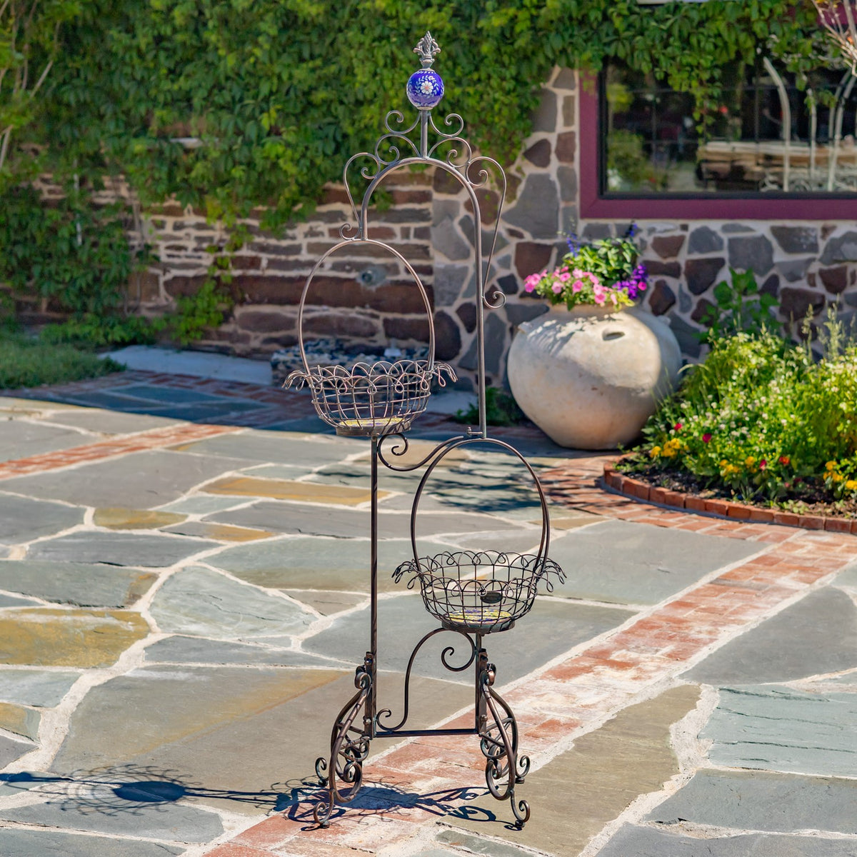Empty two-tier wire plant stand with curled scrollwork and a decorative blue finial