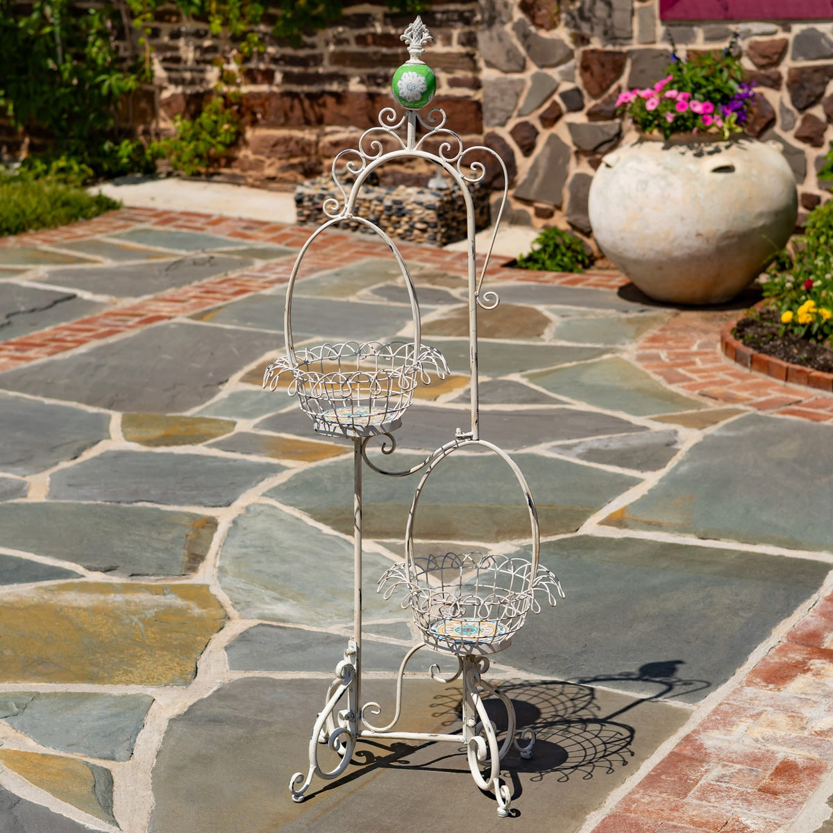 Two empty wire baskets sit at different heights on a decorative metal plant stand outdoors.