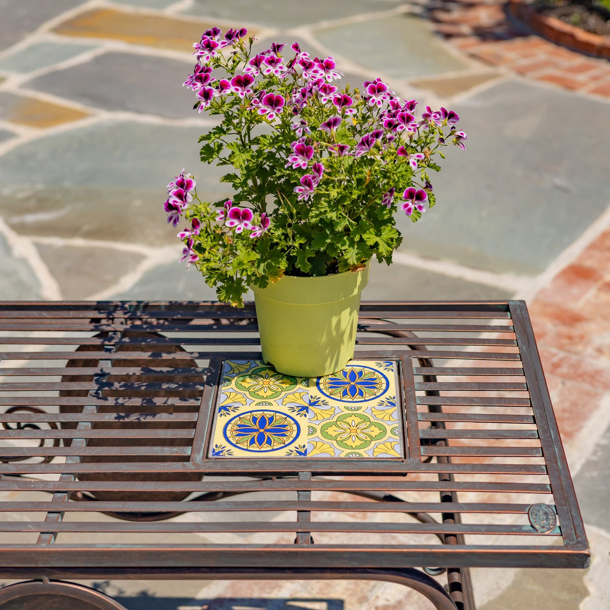 Close view of the slatted tabletop and a colorful floral mosaic inset beneath a potted plant.