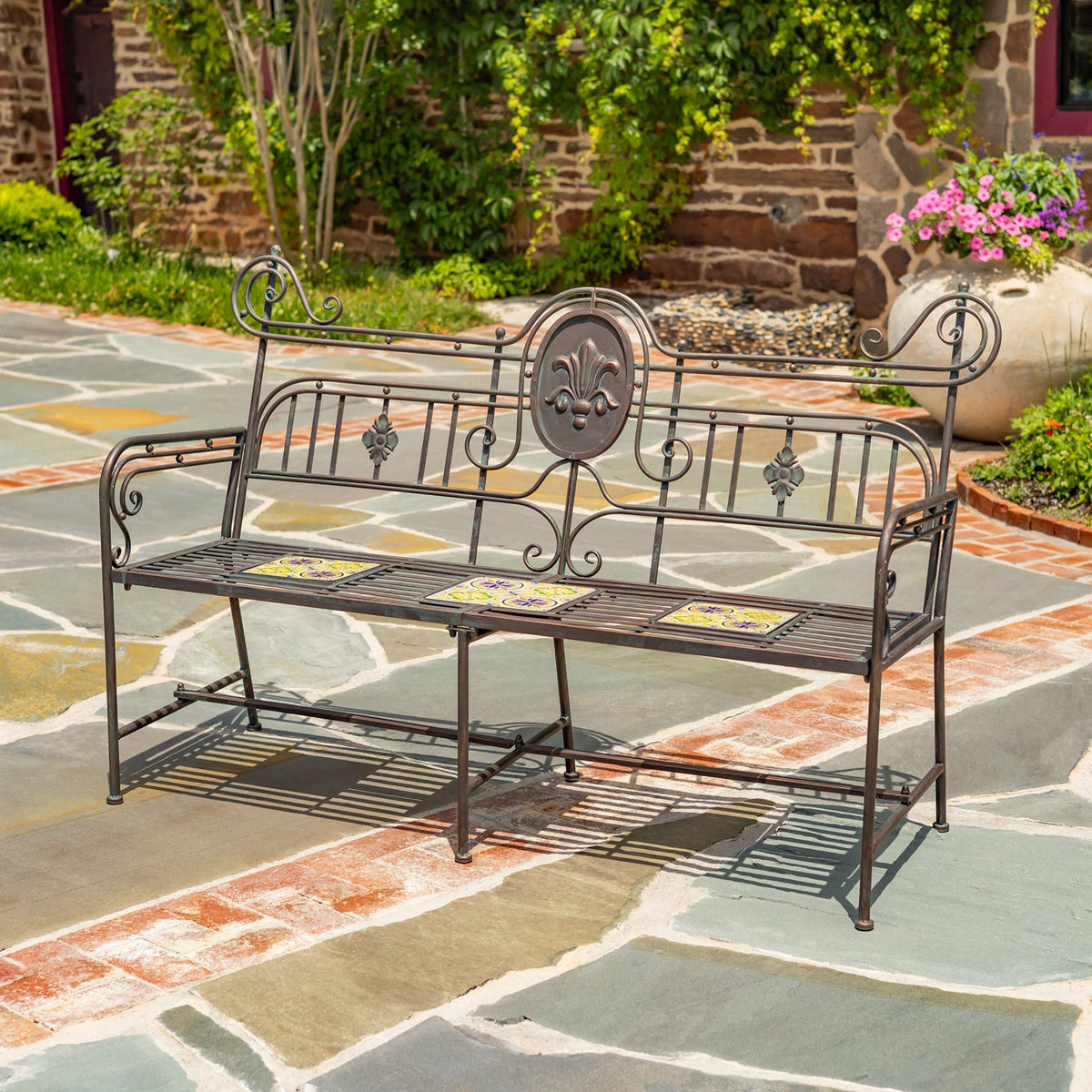 Front view of the scrolling metal bench, with floral medallion and patterned tiles across the seat.