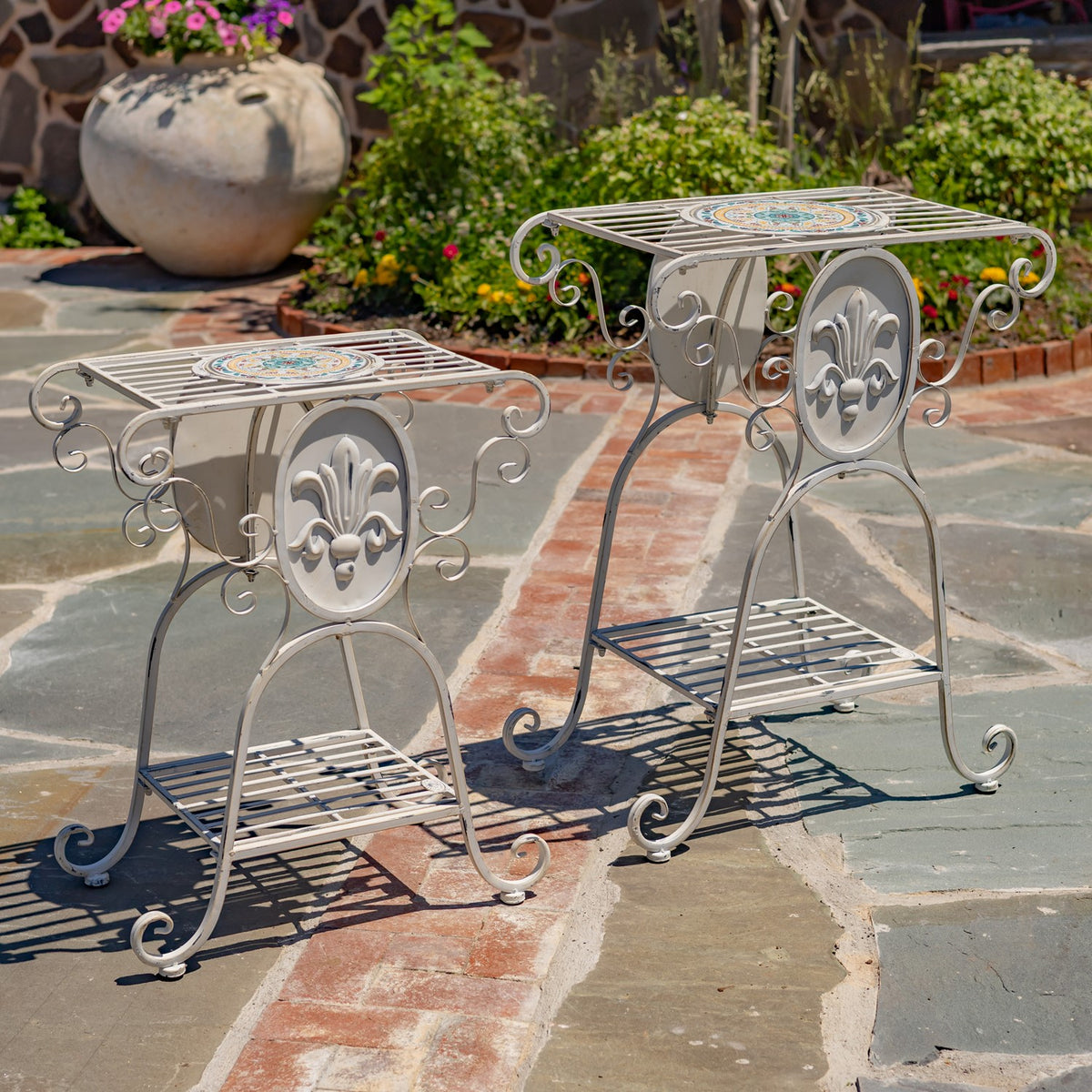 Two empty silver-toned plant stands showing their mosaic tops and lower shelves outdoors.