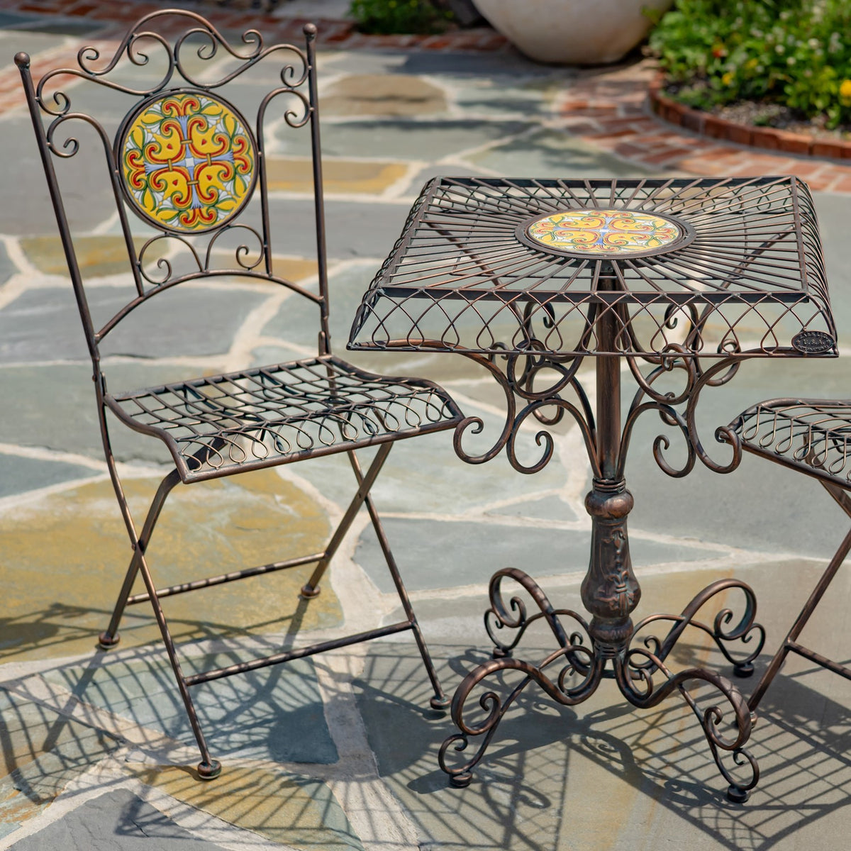 Closer view of the ironwork table and one folding chair, with a patterned mosaic inset in each.