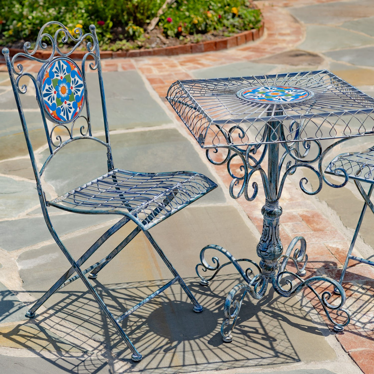One ornate metal chair beside the square table, showing their openwork frames and colorful tile accents.
