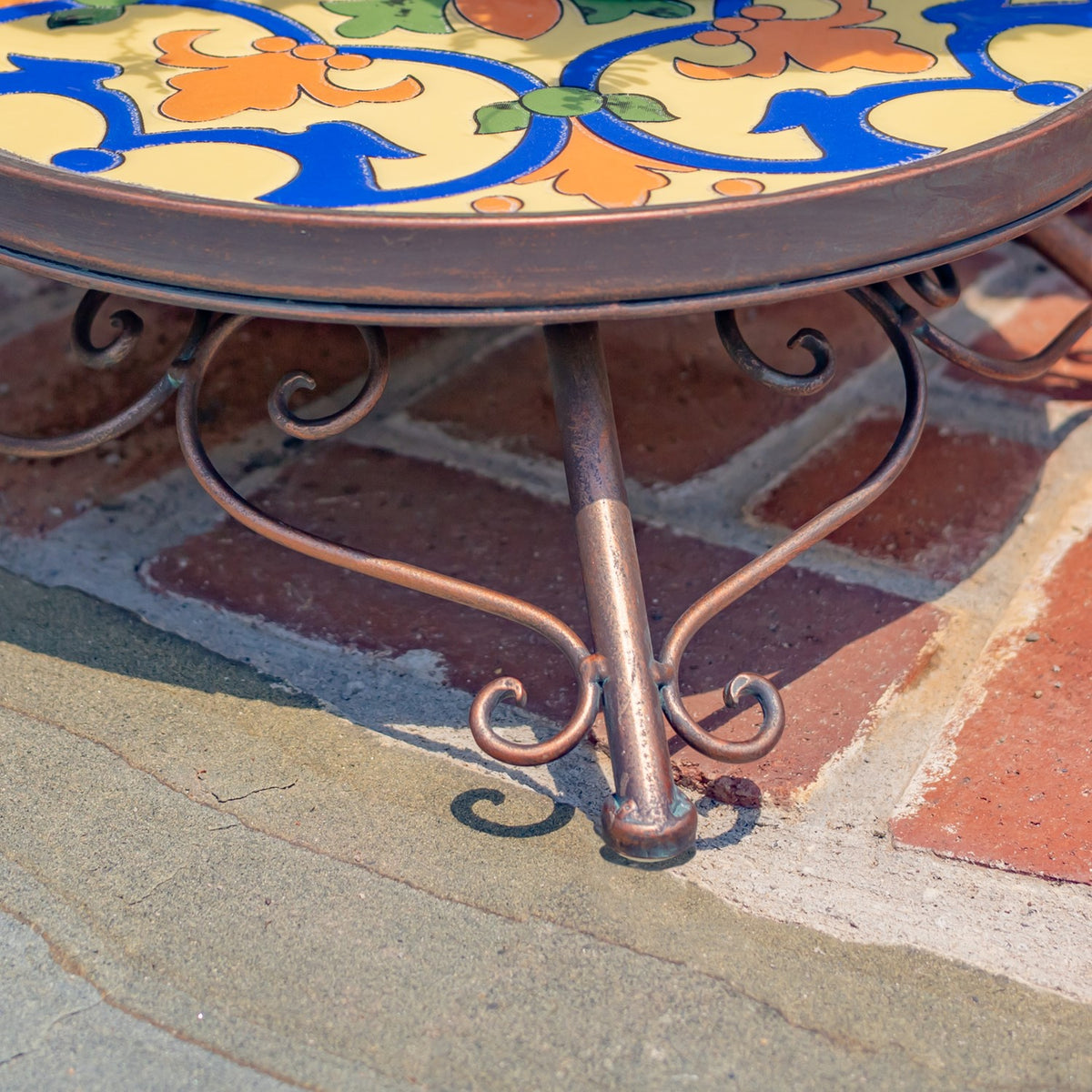 Close-up of a stand’s curved metal legs and decorative scrollwork beneath its mosaic tabletop.