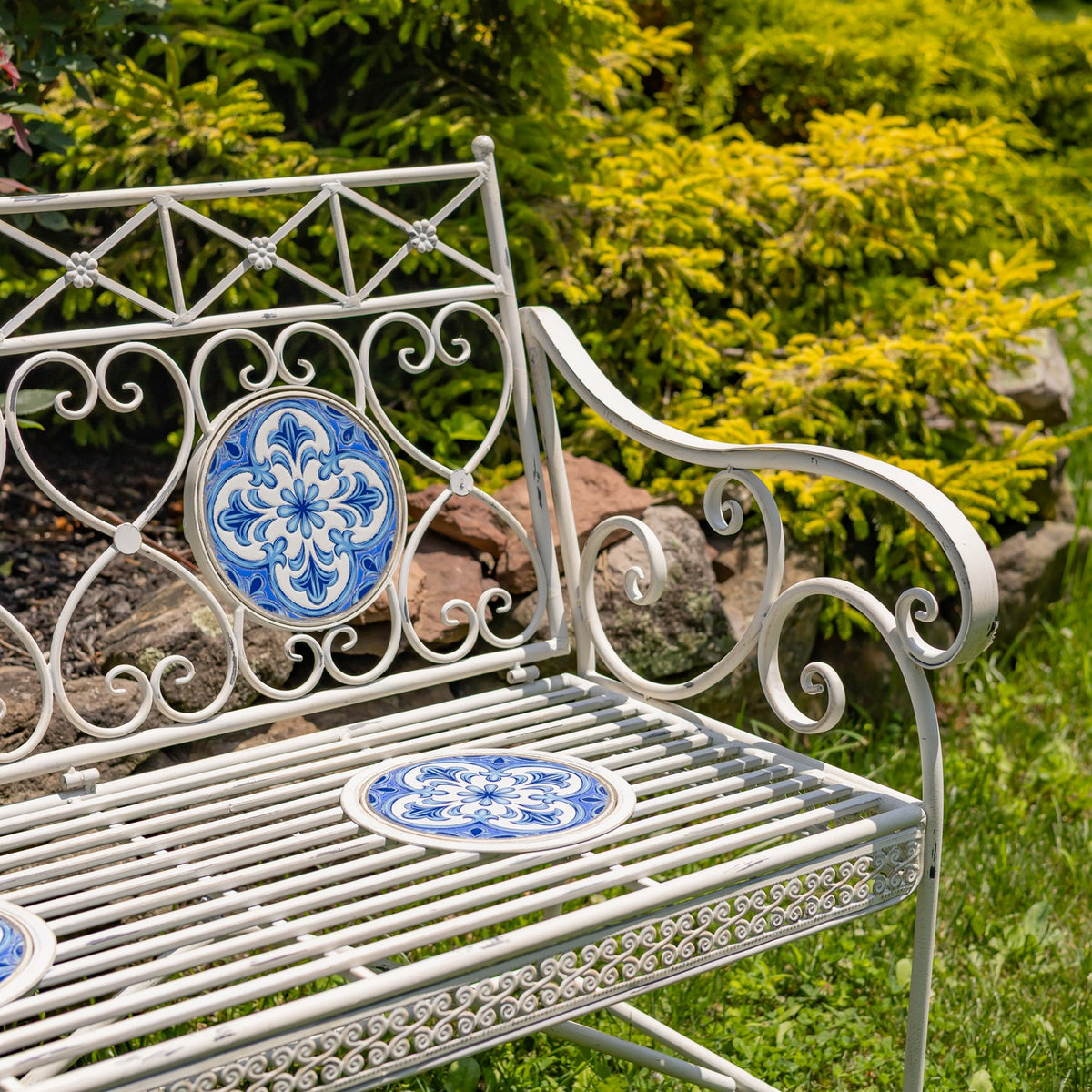 Closer view of the bench’s curled metal back and arm, blue mosaic tiles, and slatted seat.