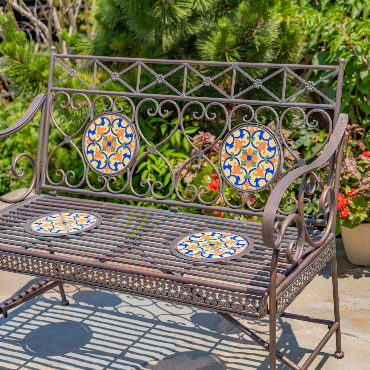 Garden bench showing its slatted seat, curled metal arms, decorative back, and four mosaic insets.