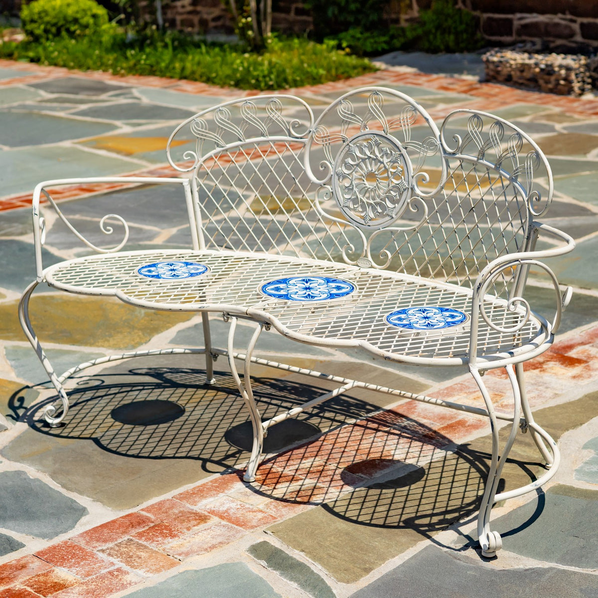 Garden bench viewed from the front corner, showing its curled arms and decorative backrest.