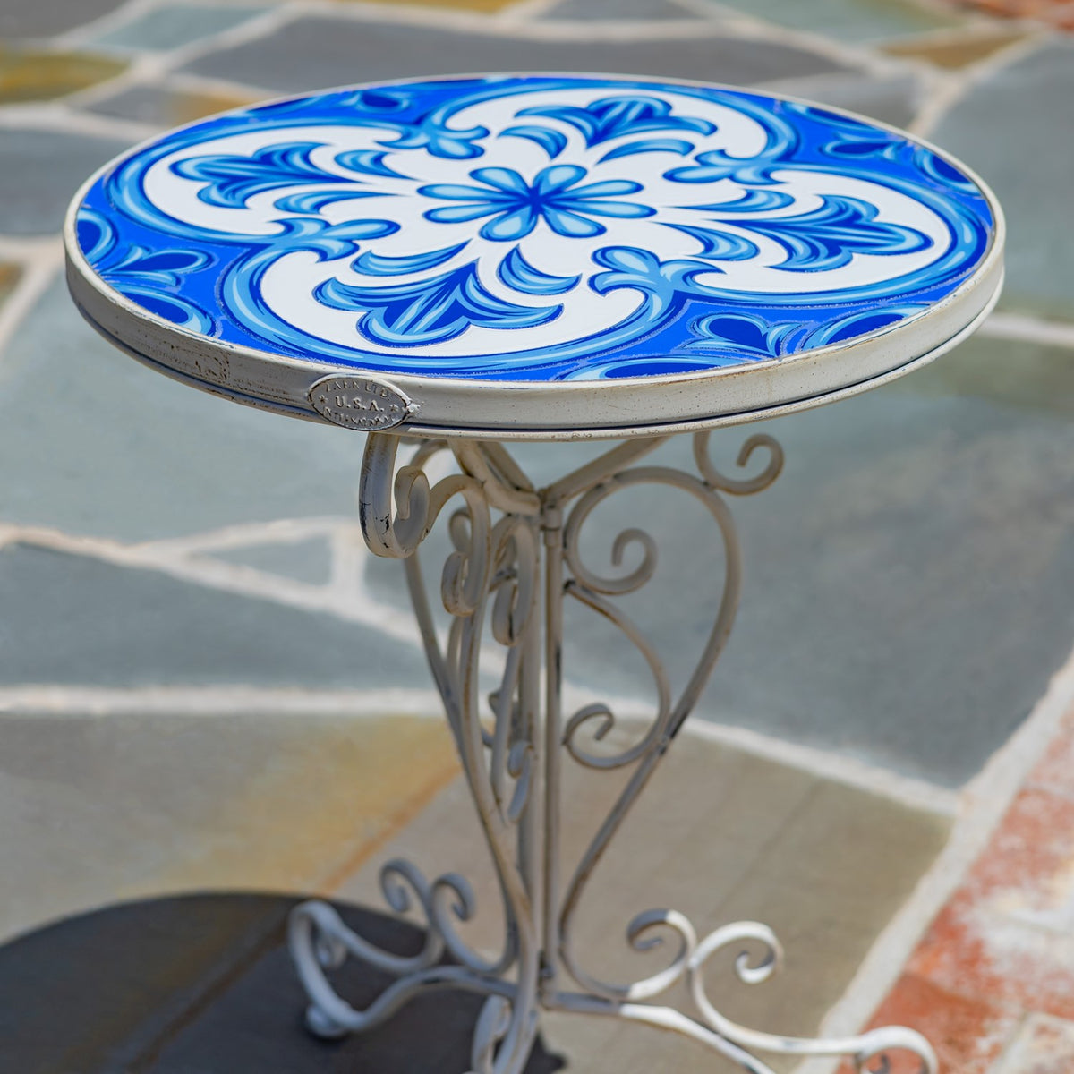 Close view of the round tabletop, showing its swirling blue-and-white mosaic pattern and ornate metal base.