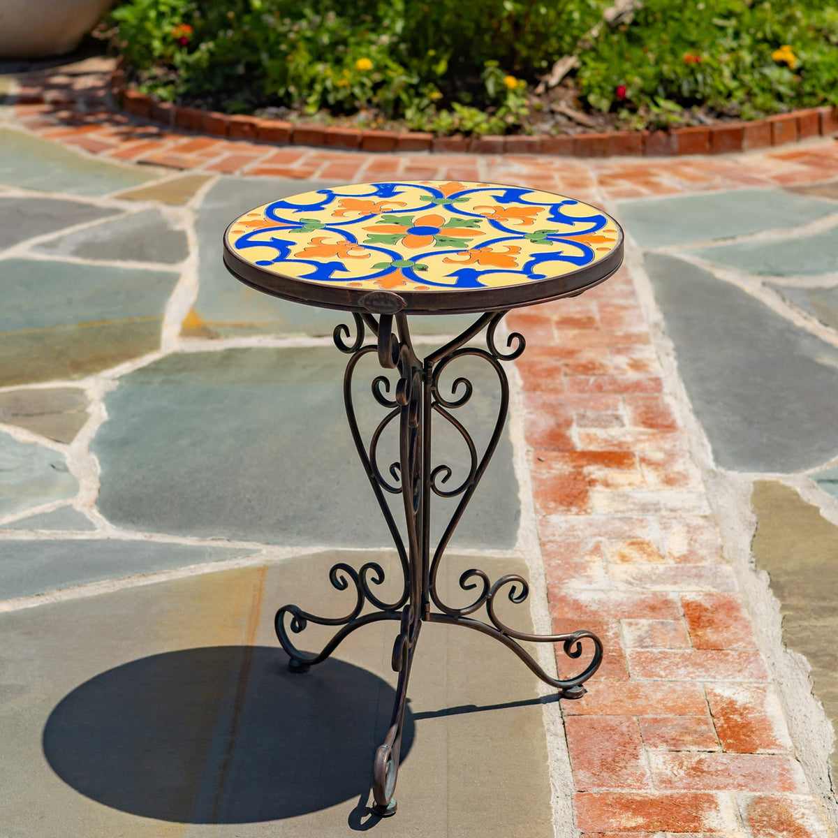 Round yellow, blue, orange, and green mosaic tabletop on an ornate dark metal stand outdoors.