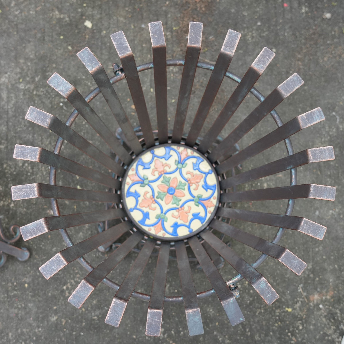 Overhead close-up of a colorful patterned tile at the center of radiating metal slats.