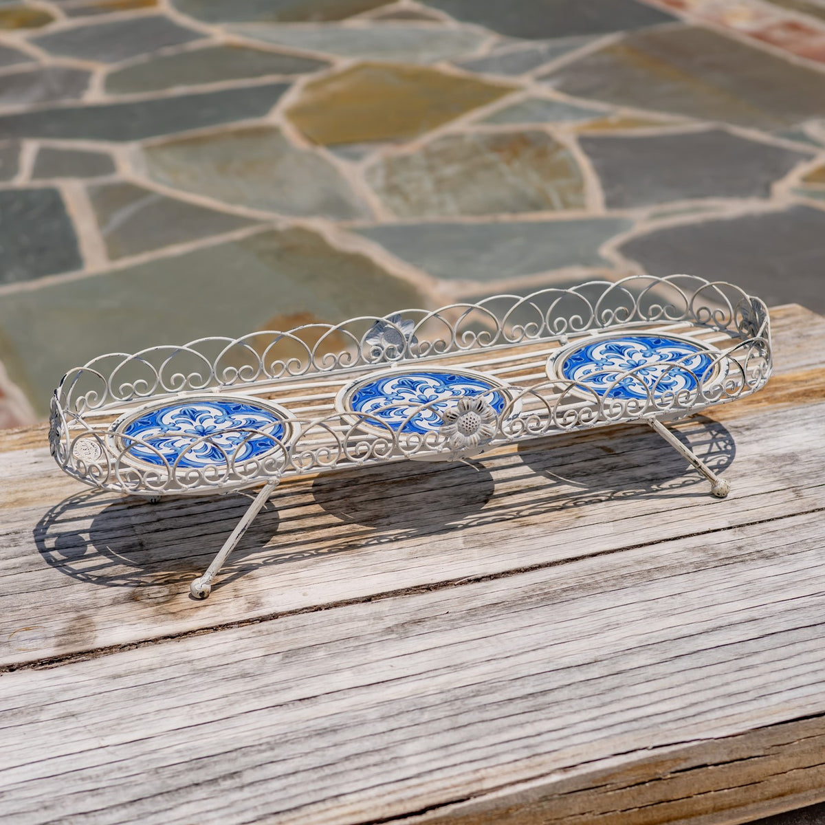 Empty white metal plant stand with blue mosaic panels and curled decorative edging.