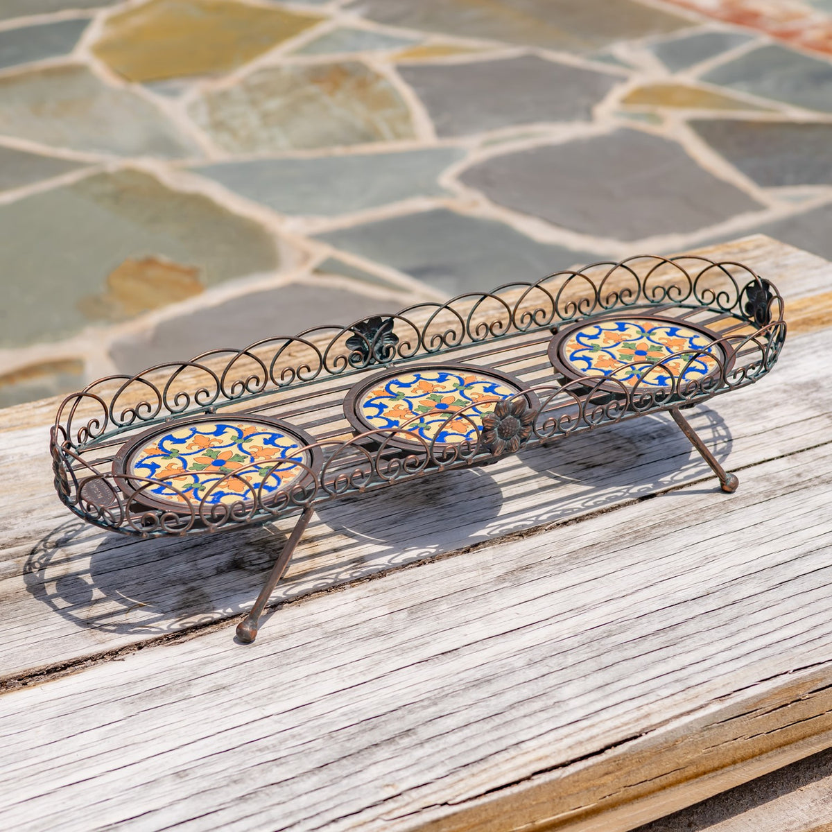 Empty bronze plant stand with three colorful circular mosaic panels and curled metal railings.