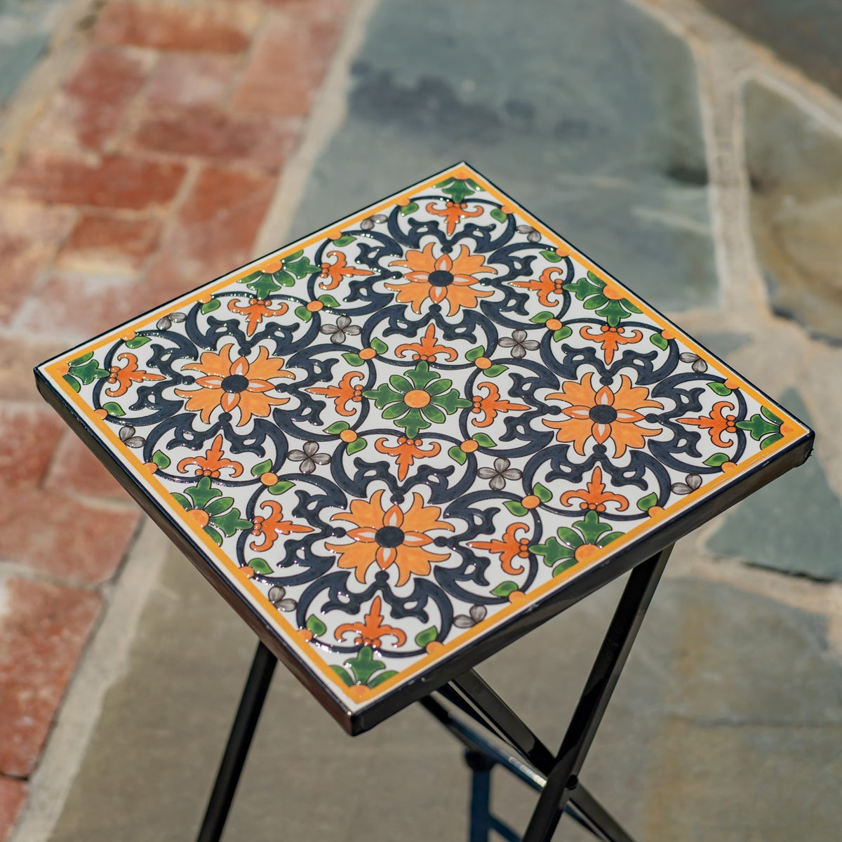 Close view of the square tabletop, decorated with an intricate orange, green, and dark floral pattern.