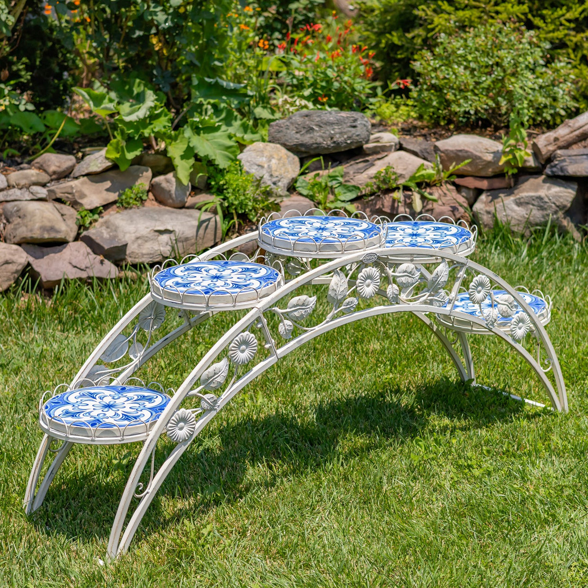 Arched white metal plant stand with four round blue-and-white mosaic platforms on grass.