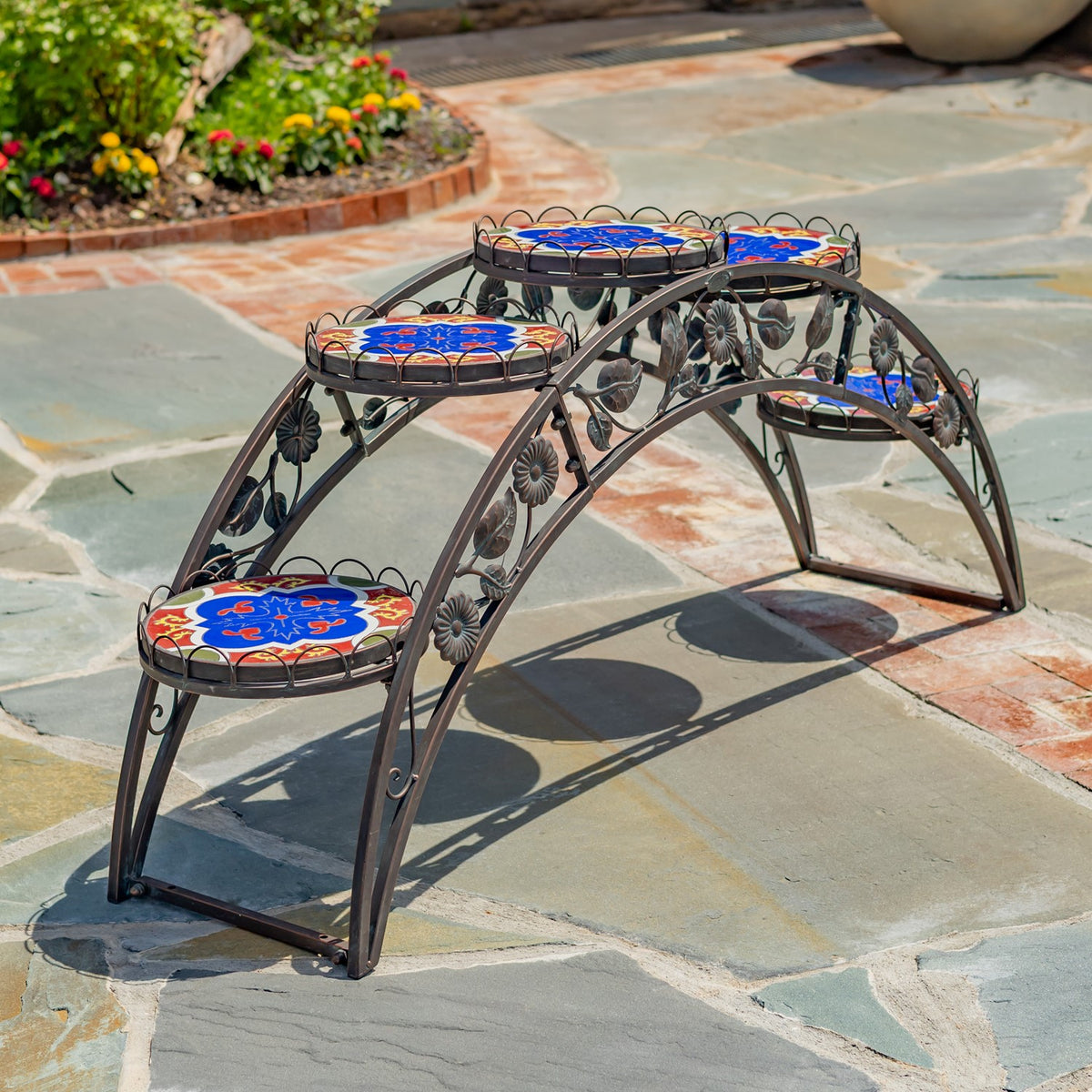 Empty arched metal plant stand with colorful round mosaic shelves on a stone patio.