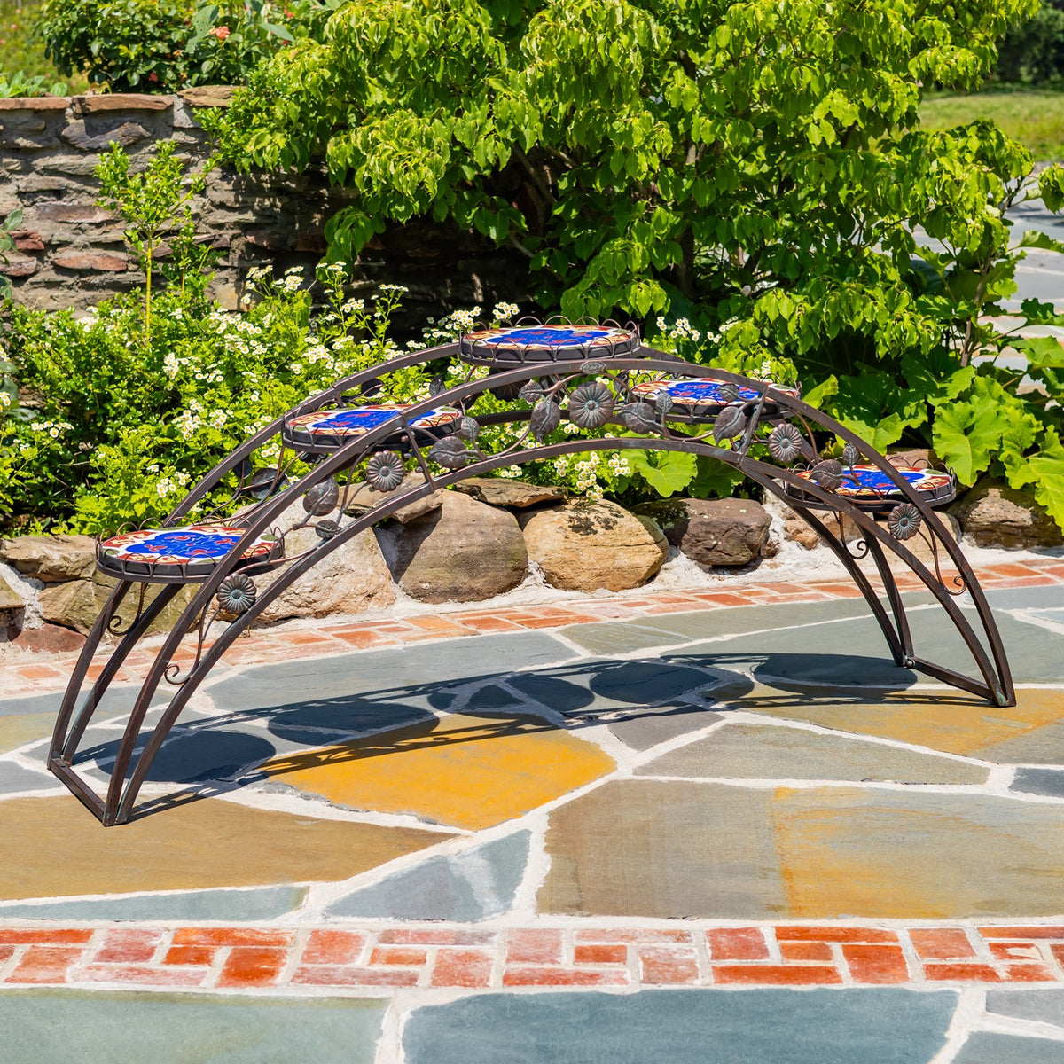 Unplanted arched metal stand with four colorful mosaic platforms on a stone garden path.