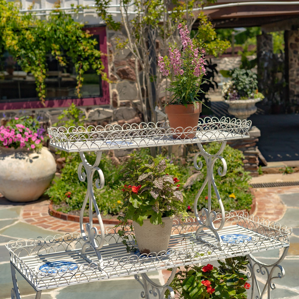 White scrollwork stand shown with two potted plants on its upper and middle tiers.