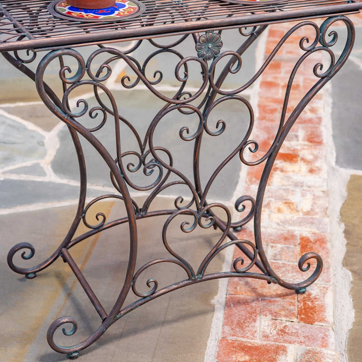 Close view of the table’s curved iron scrollwork legs and a section of its mosaic-topped surface.