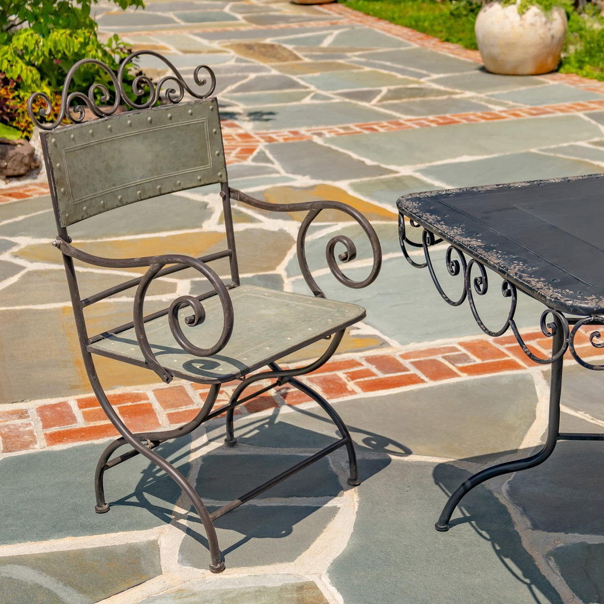 A metal dining chair beside the table, showing its scrollwork arms and curved legs.