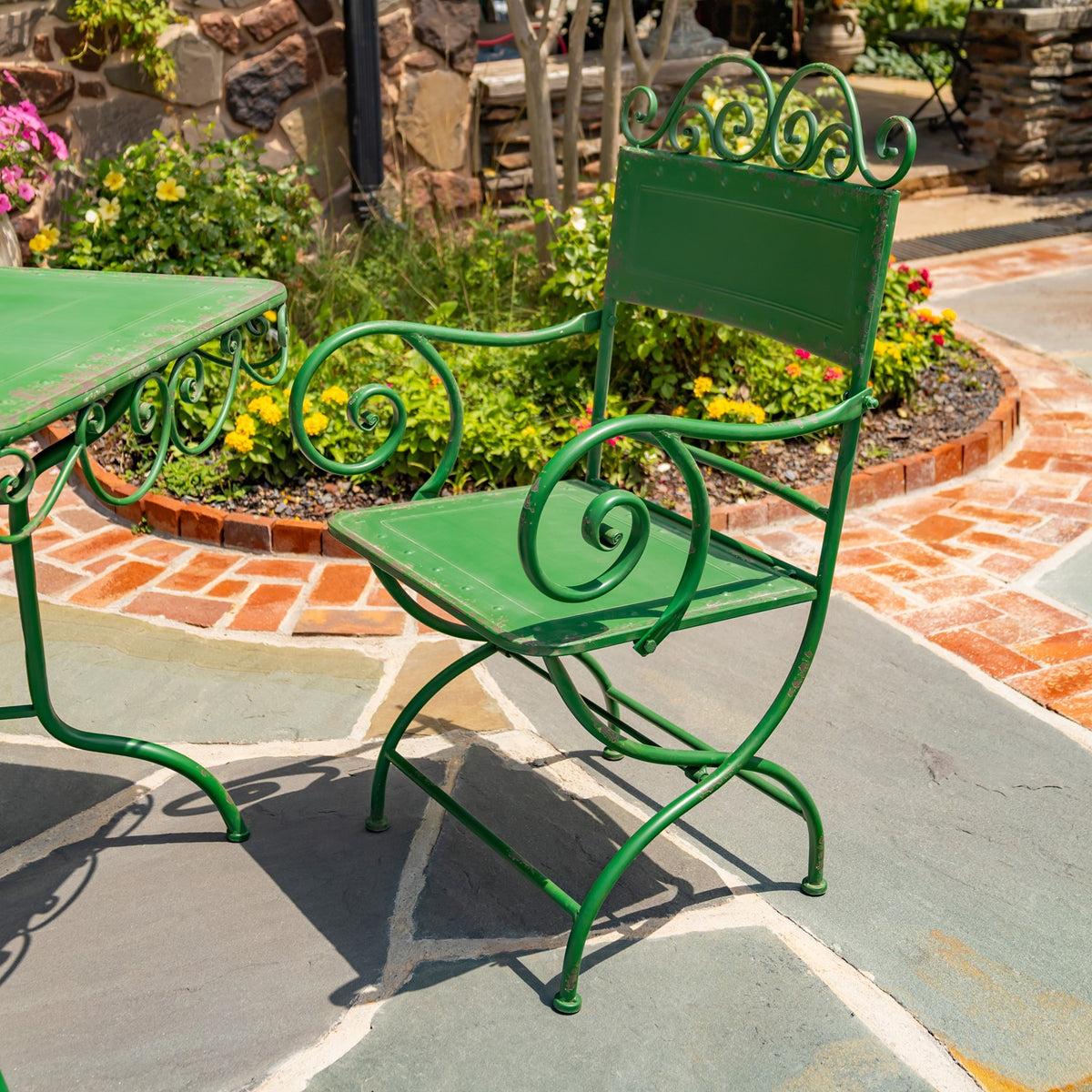 A green metal armchair with curled scrollwork beside the edge of a matching dining table.