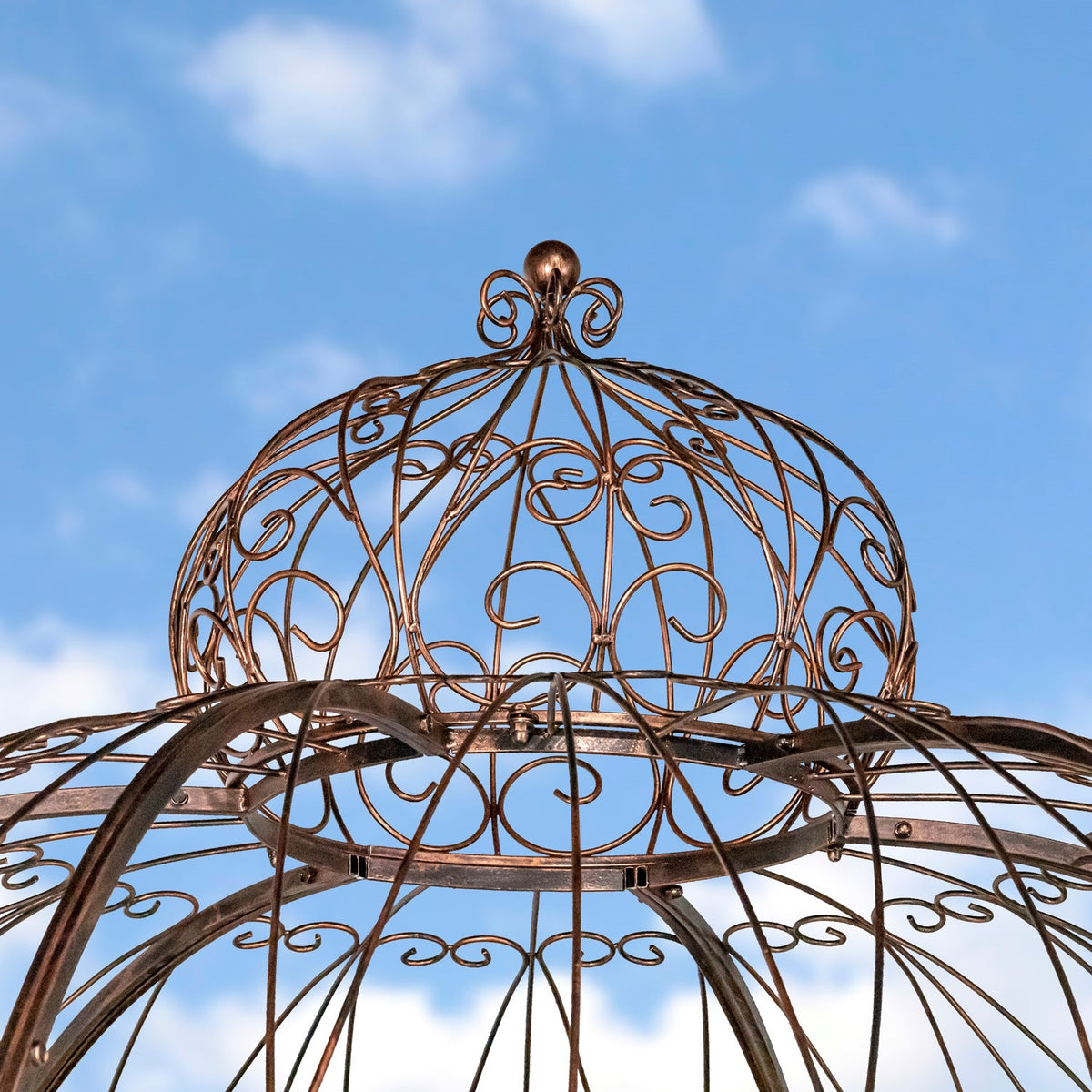 Close-up of the gazebo’s domed iron finial and curled metalwork against a blue sky.