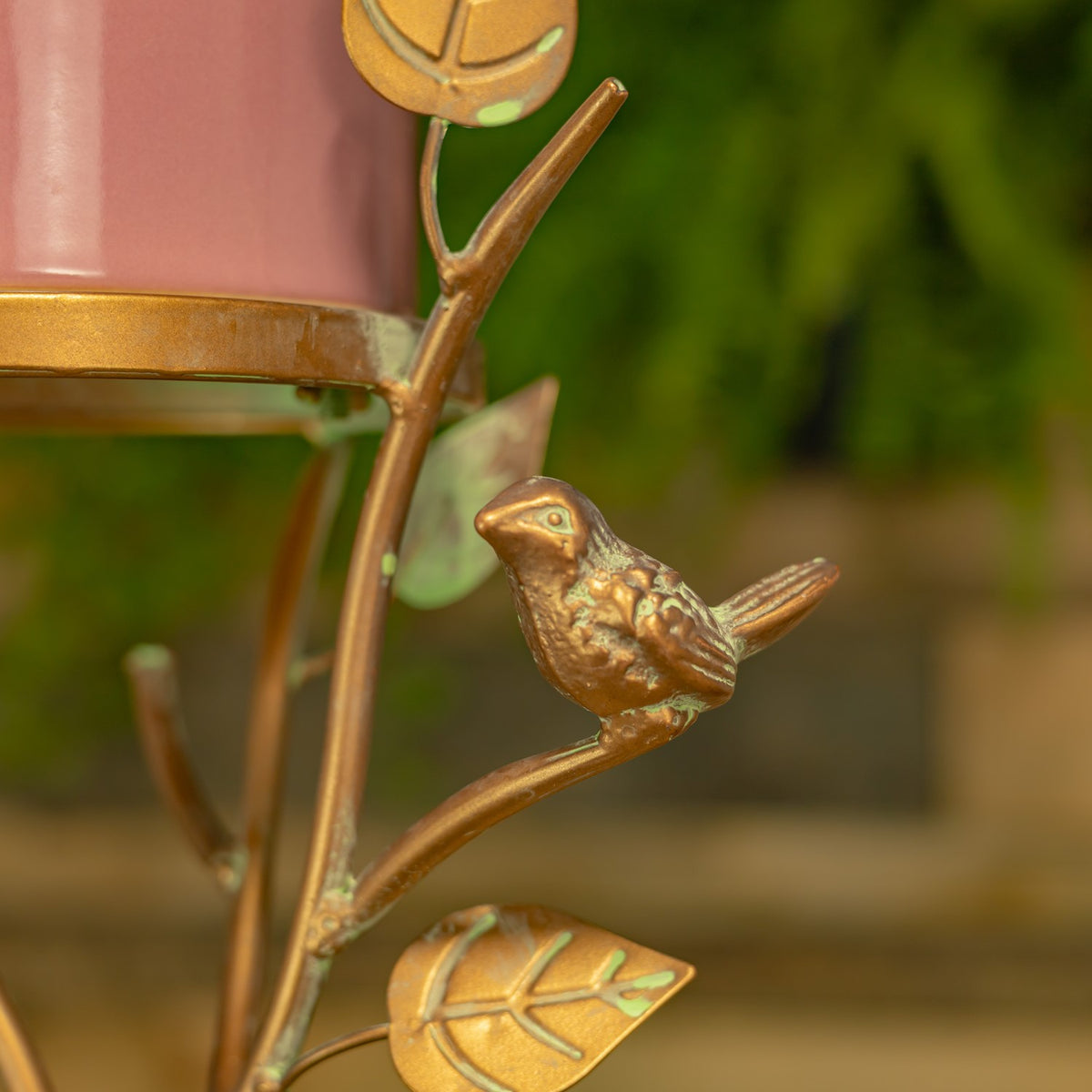 Close-up of a small gold-toned bird perched on a curved metal branch beside the pink birdhouse.
