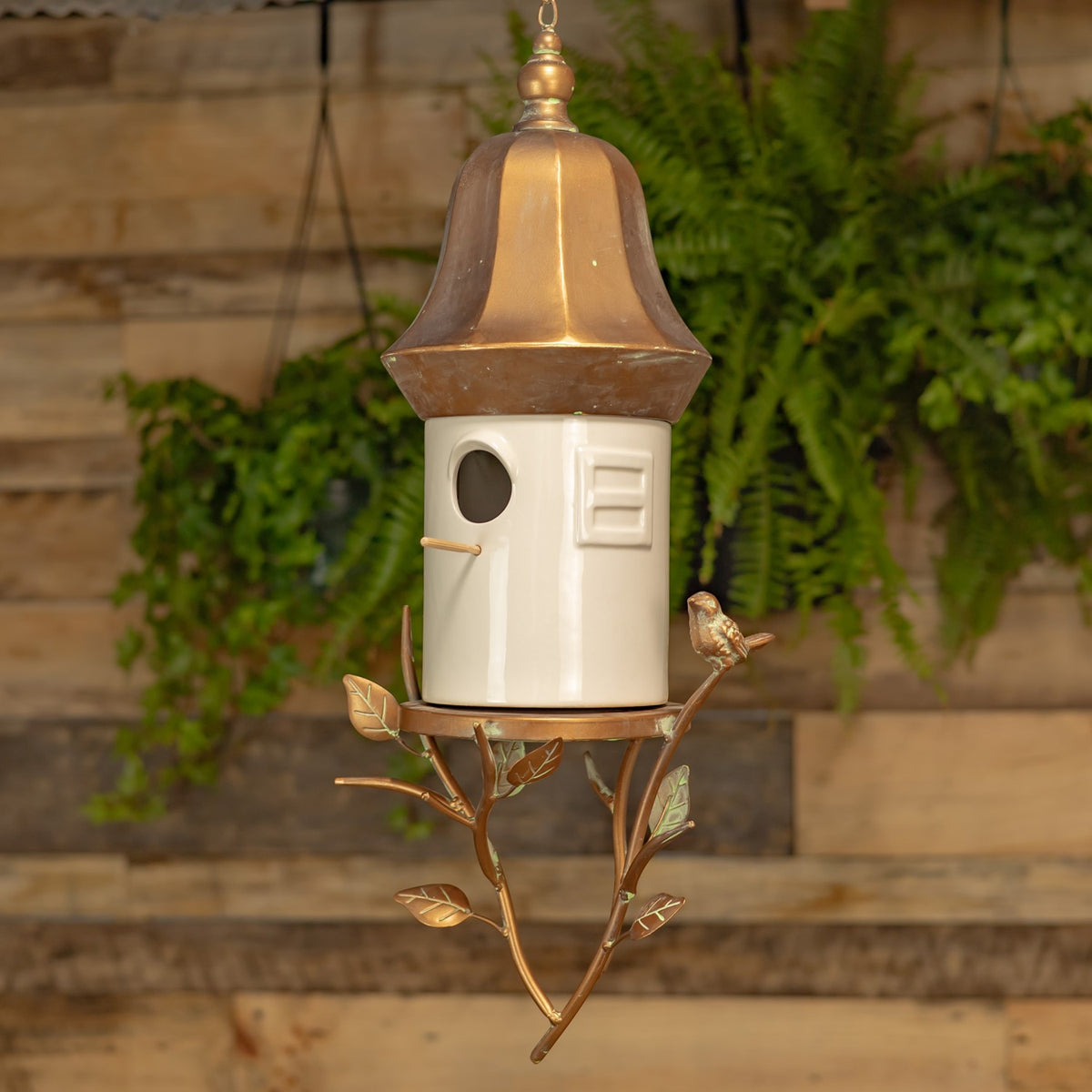 Hanging birdhouse shown in full, with a white body, copper-tone cap, and branching metal stand.