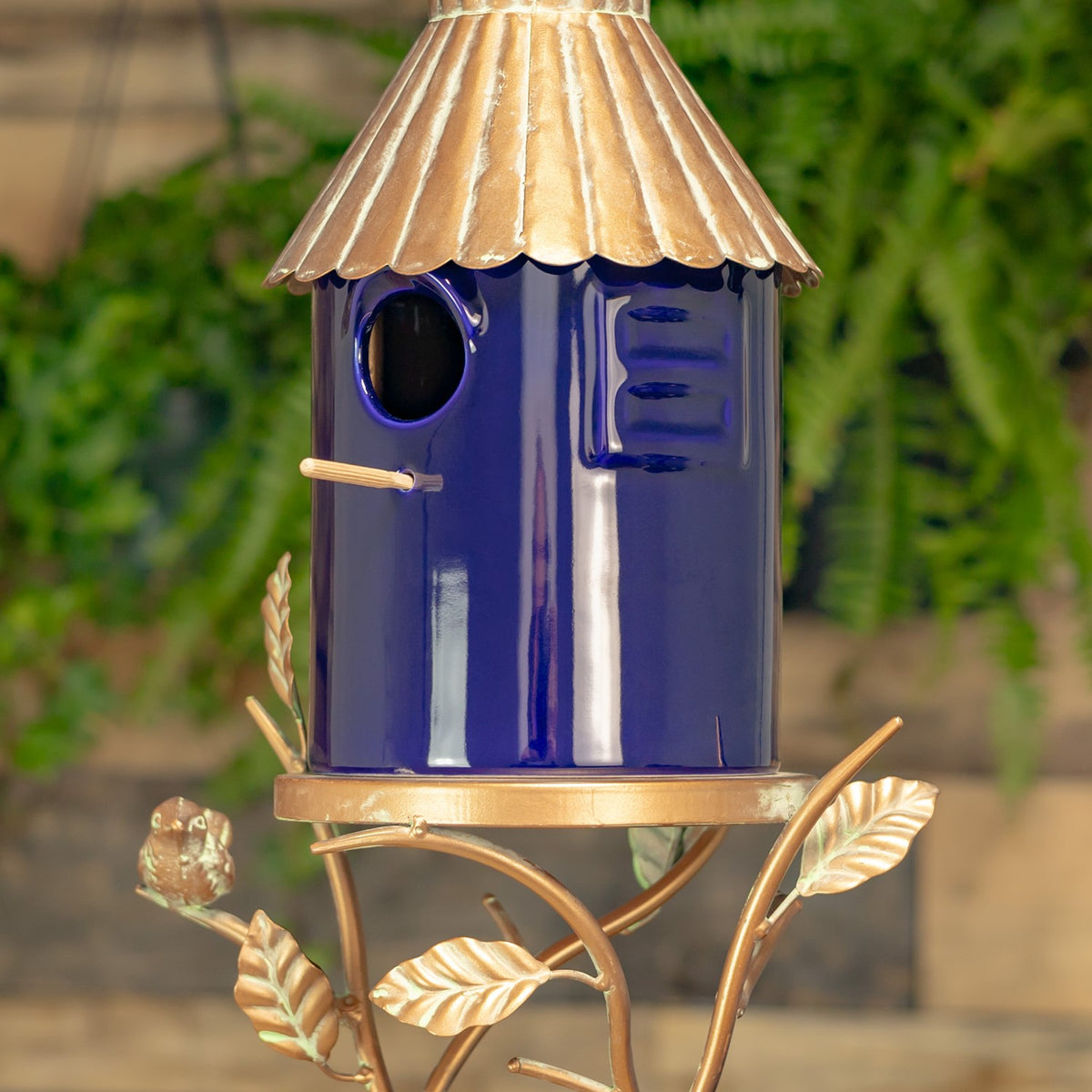 Closer view of the blue birdhouse showing its round entrance, small perch, side detail, and ridged metal roof.