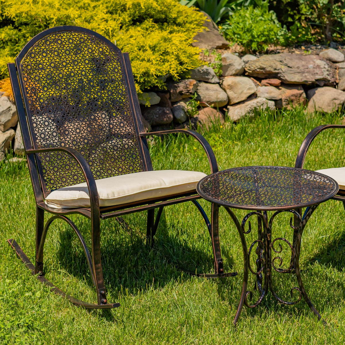 A patterned metal rocking chair with a cream cushion sits beside a round garden table.