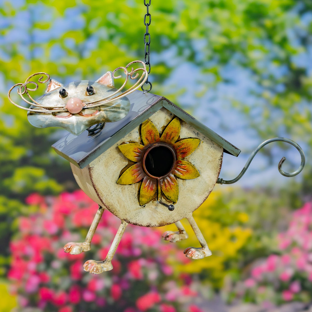 Cream cat-shaped metal birdhouse with curled whiskers and a sunflower entrance, suspended outdoors.