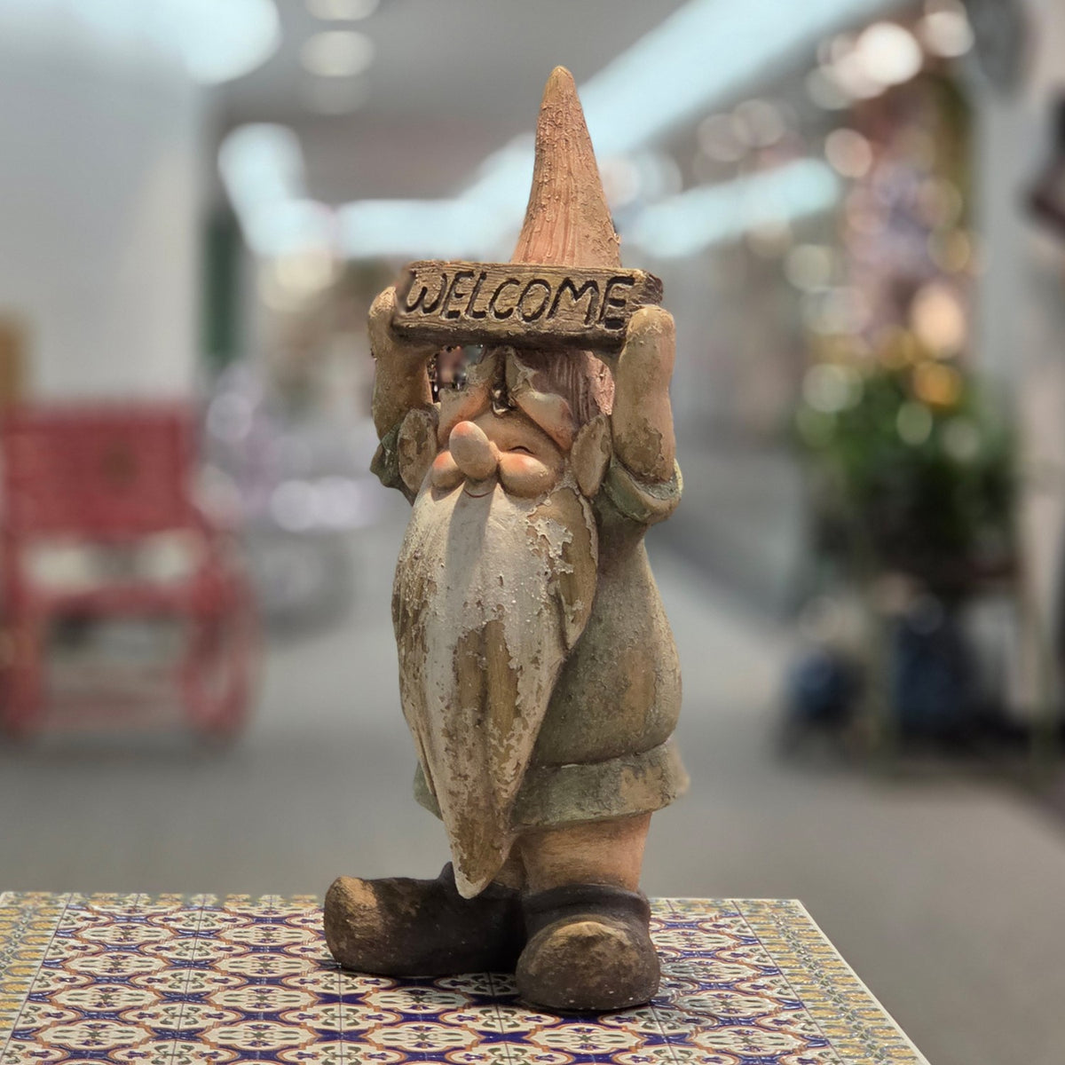 Angled front view of a garden gnome holding a welcome sign on a colorful table