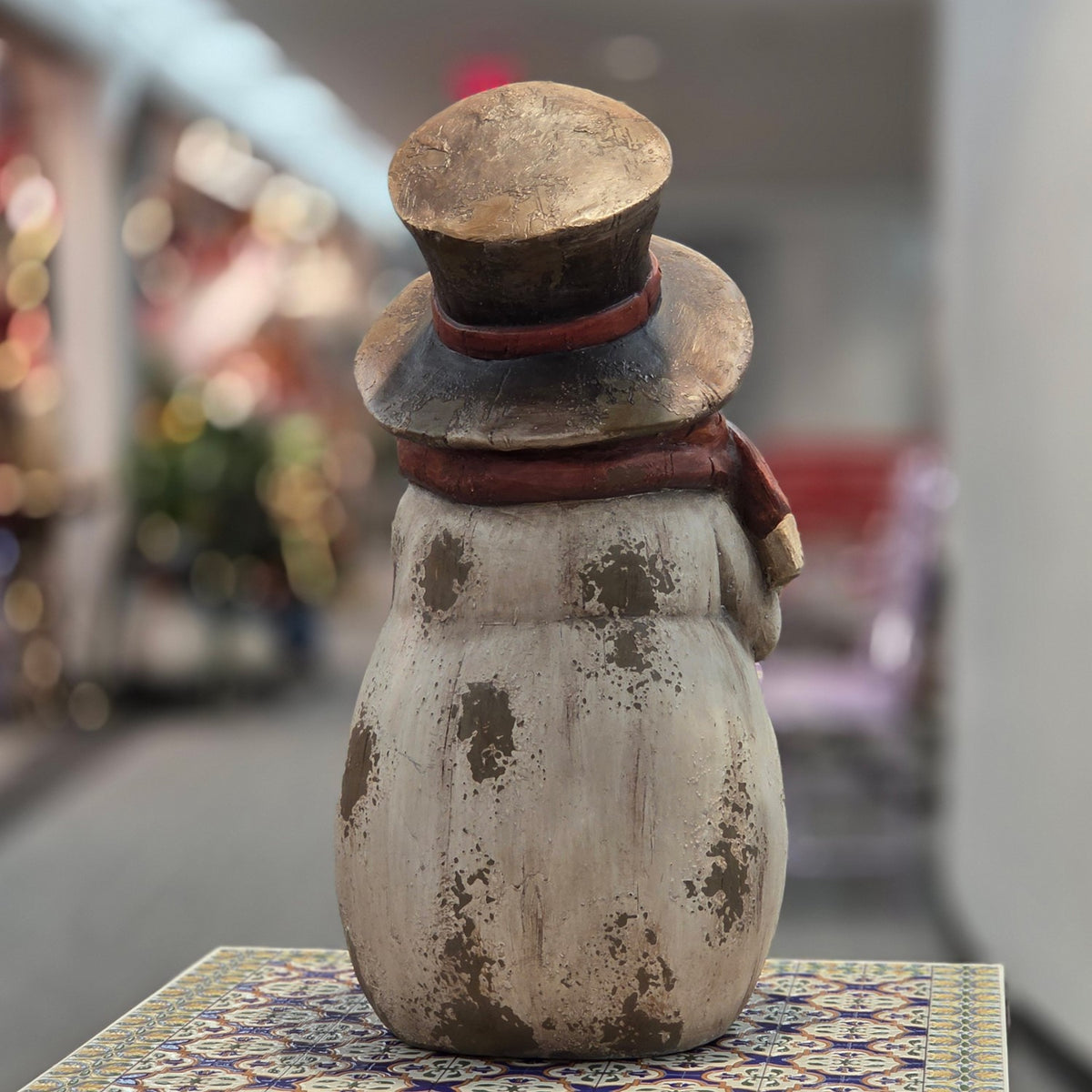 Back view of a distressed snowman figurine wearing a tall brown top hat and scarf