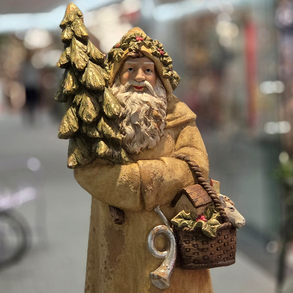 Closer front view of Santa holding a tree beside a basket of holiday items