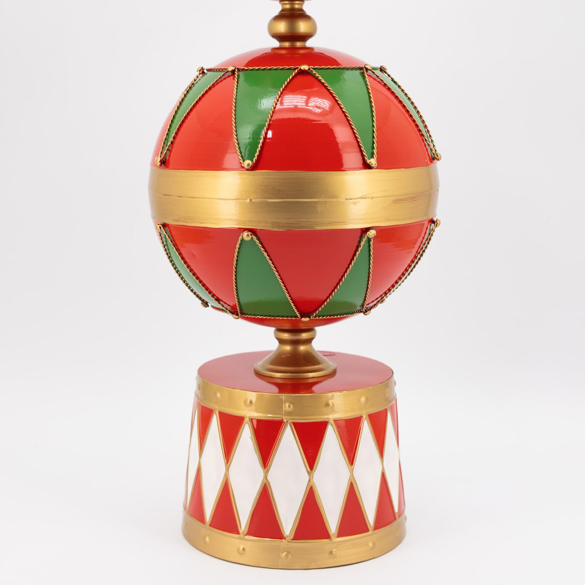 Close-up of a red, green, and gold sphere above a red-and-white diamond-patterned base.