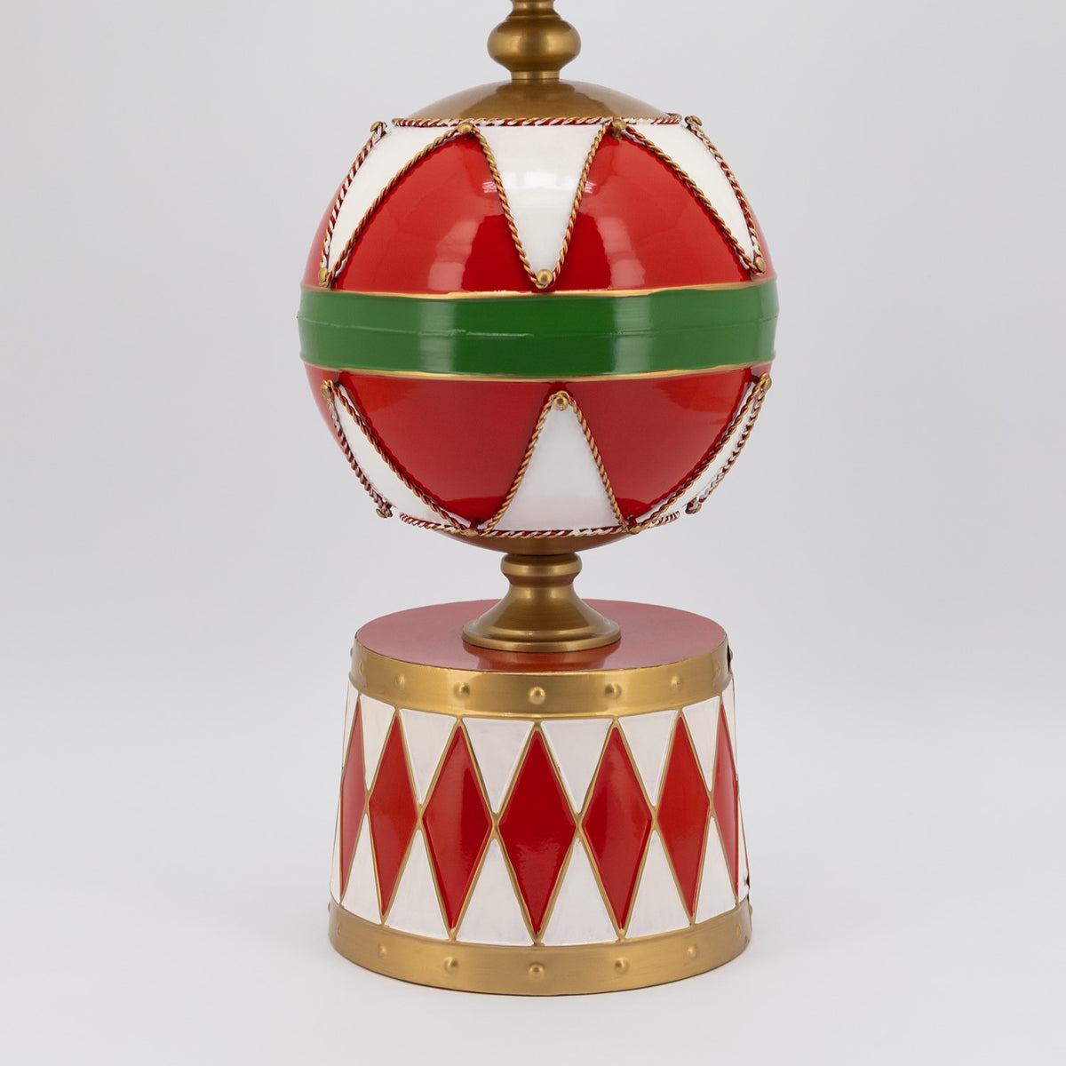 Close view of a red sphere with a green band above a white base patterned with red diamonds and gold trim.