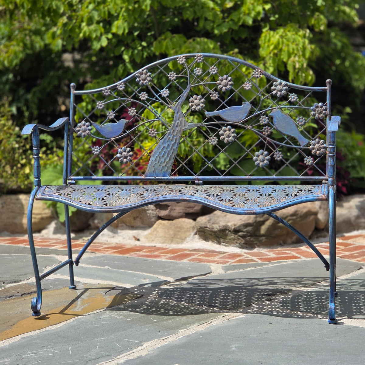 Dark metal bench showing its curved seat and decorative tree, birds, and flowers on the backrest.