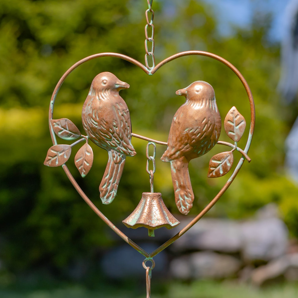 Two sculpted birds face each other inside a heart frame, with leaf accents and a small bell below.
