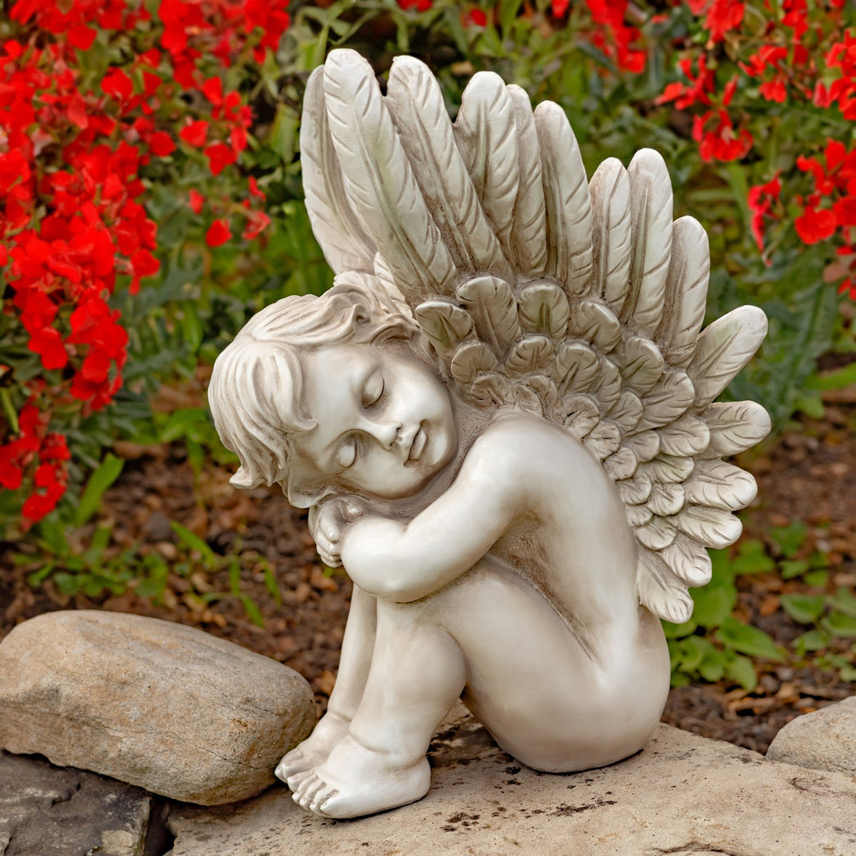 Antique grey sitting cherub statue beside a rock in a flower garden