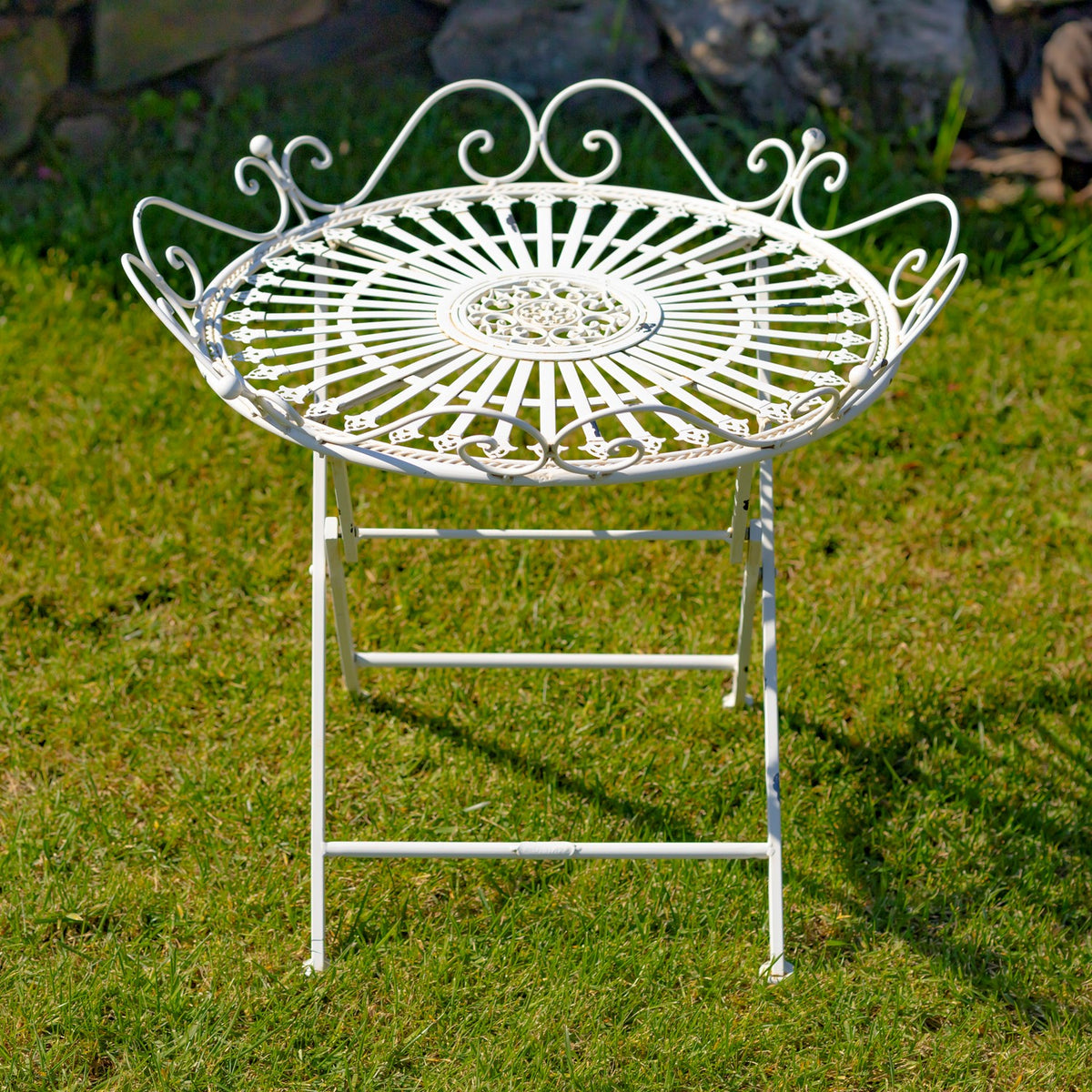 White ornate round iron garden table standing on grass, with a radial top and curled rim details.