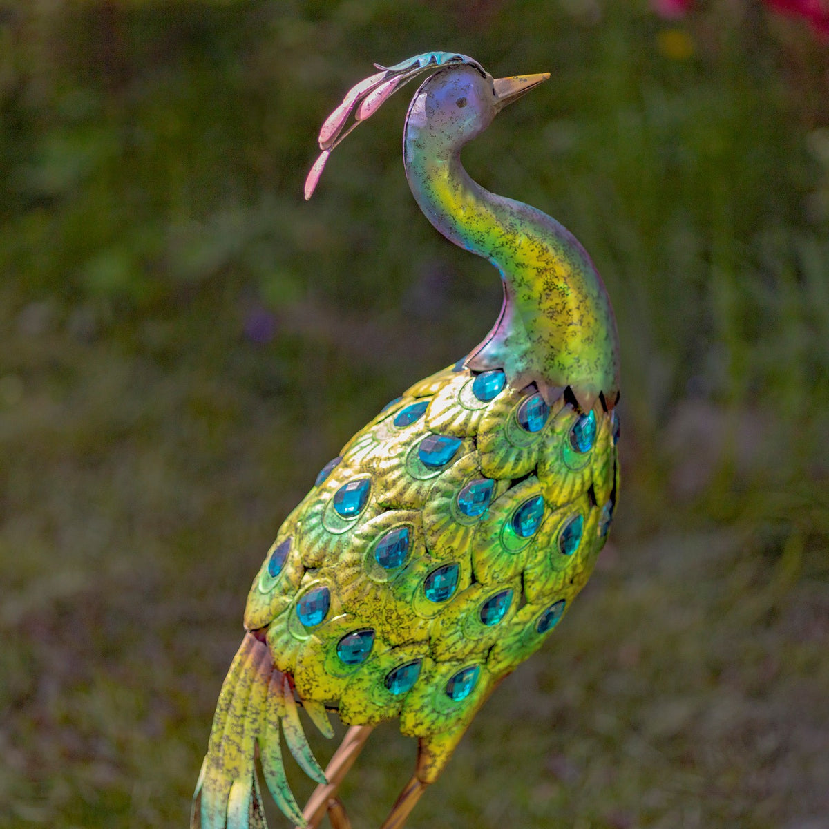 Close view of a peacock statue with blue gems and green metal feathers